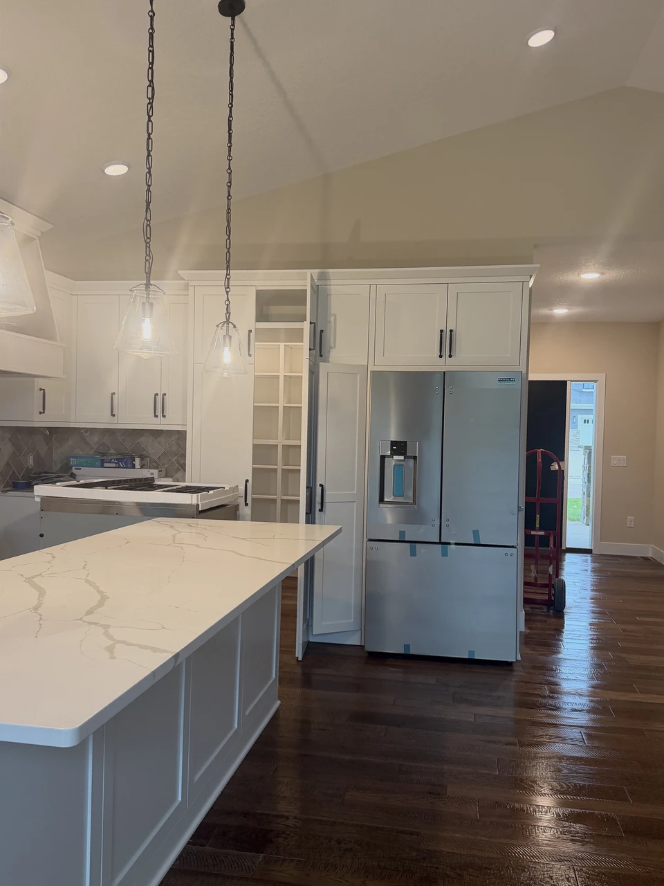 Kitchen with a white island, pendant lights, refrigerator, and wood flooring, photographed by Delia